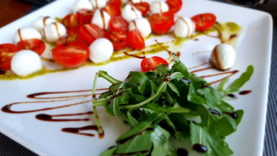 Fresh Caprese salad with ripe tomatoes, mozzarella, basil, and drizzled balsamic glaze on a rustic wooden table.