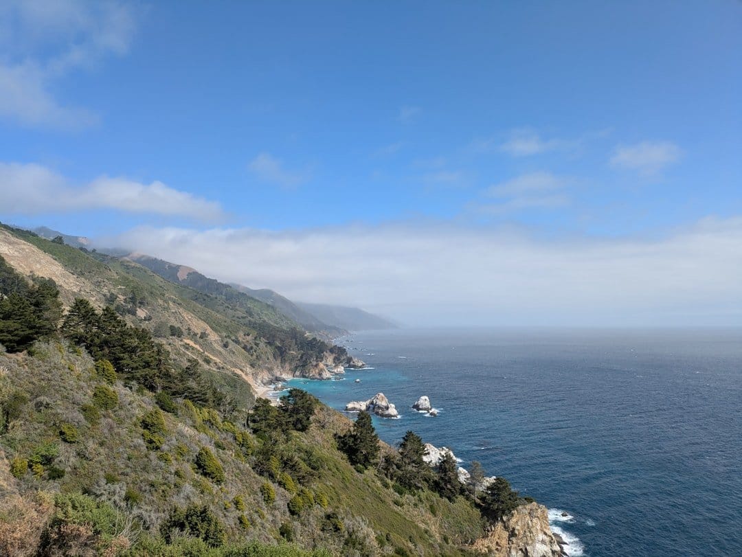 Scenic view of the Pacific Coast Highway with cliffs, ocean waves, and a winding road, perfect for a road trip.