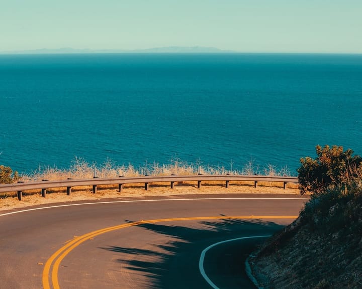 A scenic view of the Pacific Coast Highway with cliffs, ocean waves, and a winding road, perfect for a road trip.