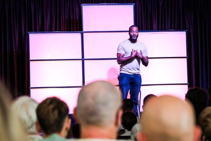 Justin Pearson speaking at a podium, addressing concerns about AI, with a backdrop featuring Elon Musk and tech imagery.