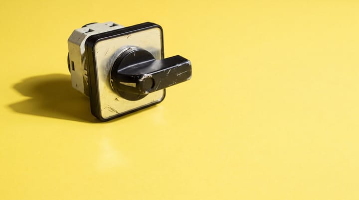 Worn industrial rotary changeover switch with black handle resting on a bright yellow seamless background.