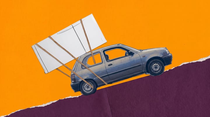 Small gray hatchback hauls an oversized white refrigerator up a steep purple hillside beneath an orange sky.